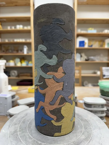 어두운 원통 표면에 여러 색의 동물 형상이 있는 도자 작품